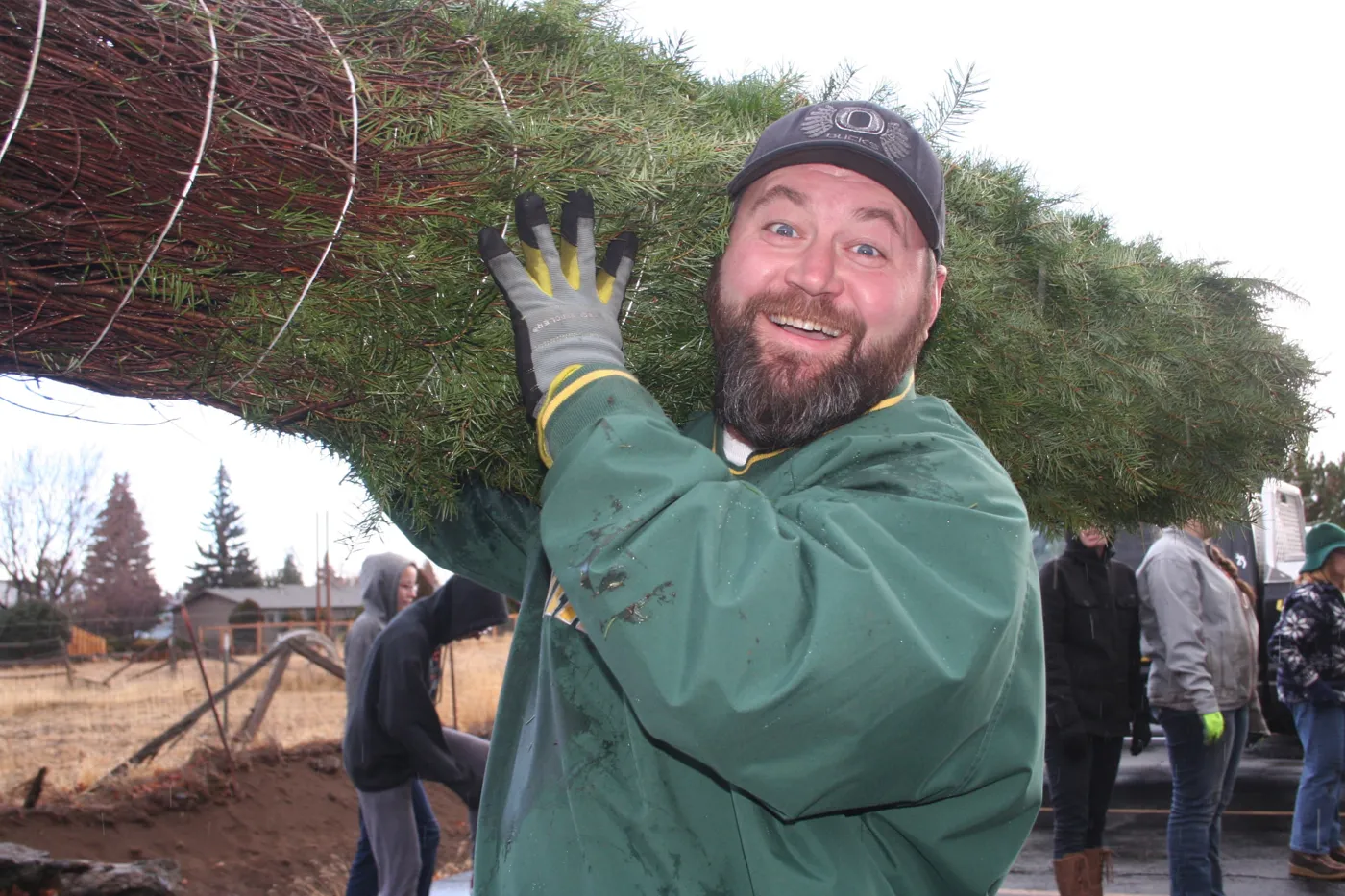 Keith Leitz smiling while carrying a large tree on his shoulder
